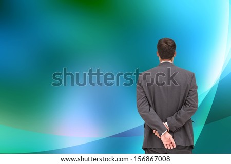 Composite image of businessman standing with hands behind back looking at blue and green abstract background