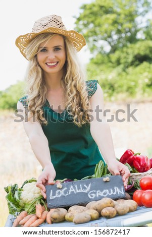 Smiling young female farmer standing at her stall in the farmers market while looking at the camera
