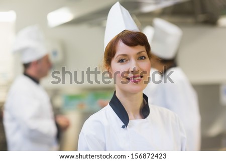 Smiling female chef posing in a kitchen while wearing a uniform