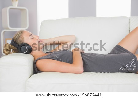 Casual calm blonde lying on couch listening to music in bright living room