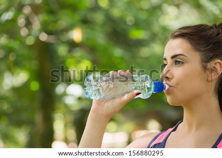 Sporty woman drinking water outdoors in a forest on a sunny day