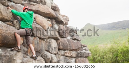 Determined man climbing a large rock face with mountains in the background