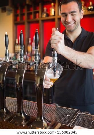 Handsome Barkeeper Pulling A Pint Of Beer And Smiling Behind The Bar