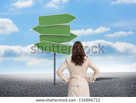 Composite image of businesswoman standing back to camera looking at green road signs