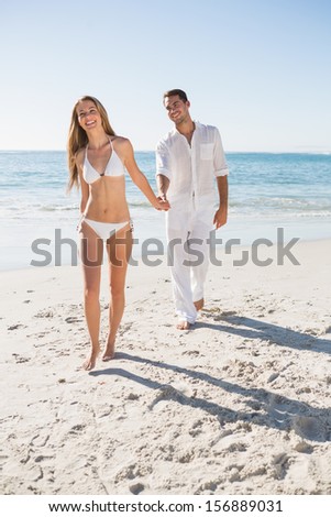 Smiling blonde walking away from man holding her hand on the beach