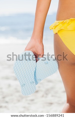 Woman in yellow bikini holding flip flops rear view on beach