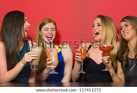 Chatting friends holding cocktails and laughing in a nightclub