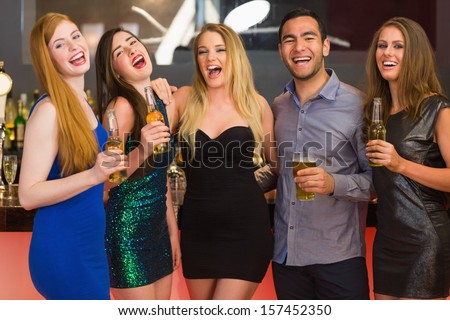 Laughing friends holding beers posing and looking at camera in the nightclub