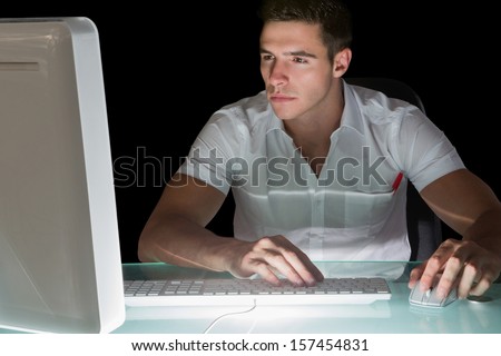 Handsome focused computer engineer working at night at his lit desk