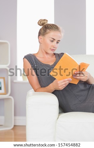 Casual calm blonde relaxing on couch reading a book in bright living room