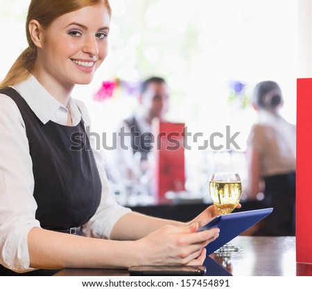 Attractive businesswoman holding tablet and wine glass and smiling at camera in a restaurant