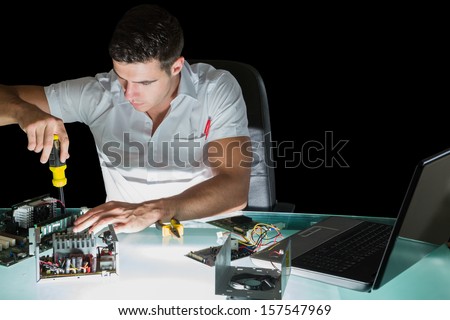 Handsome stern computer engineer working by night with screw driver at his lit desk