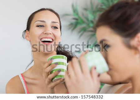 Young laughing woman having coffee with friend on the couch at home