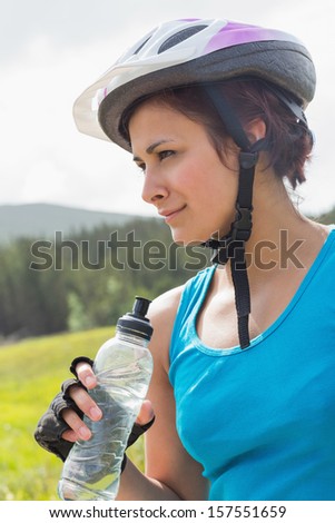 Fit woman wearing bike helmet holding water bottle in the countryside