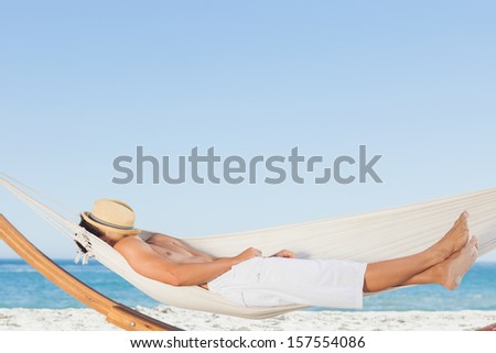 Man wearing straw hat relaxing in a hammock on the beach on holidays