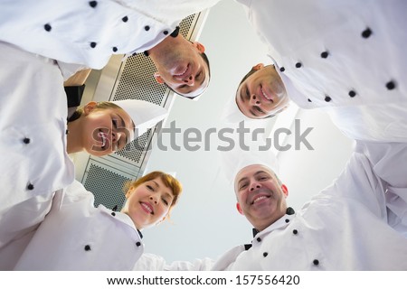Five chefs standing in a circle wearing uniforms in a kitchen