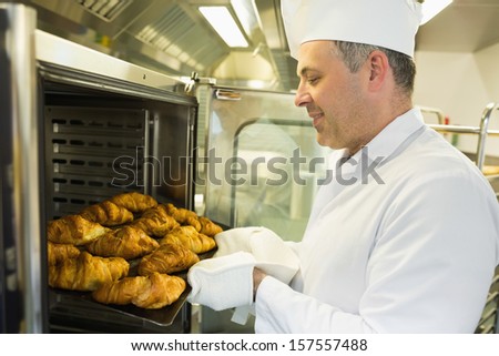 Mature baker putting some croissants into an oven wearing a uniform