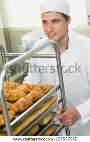 Handsome happy baker pushing a trolley with food on it