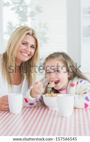 Little girl eating cereal at breakfast with her mother in kitchen