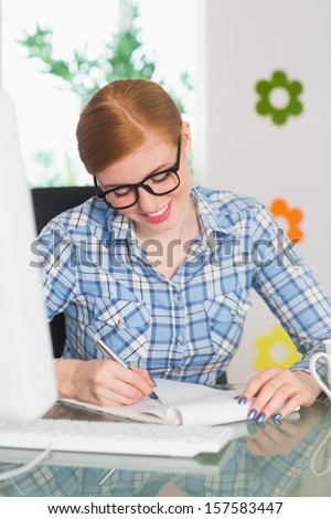 Happy redhead writing on notepad at her desk working from home