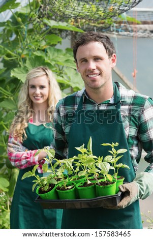 Man holding carton of small plants and looking at the camera with girlfriend behind him