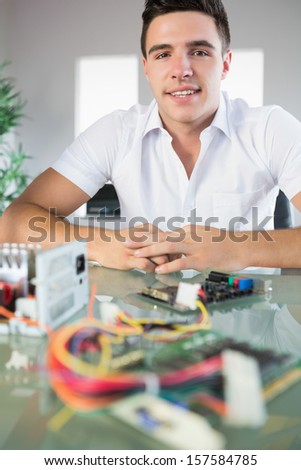 Attractive computer engineer sitting at desk looking at camera in bright office
