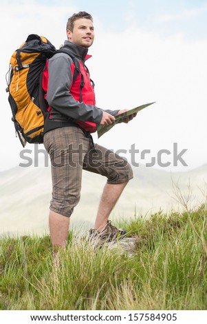 Handsome hiker with rucksack walking uphill holding a map in the countryside