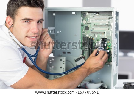 Smiling computer engineer examining hardware with stethoscope in bright office