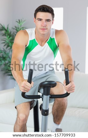 Handsome man training on exercise bike in bright living room