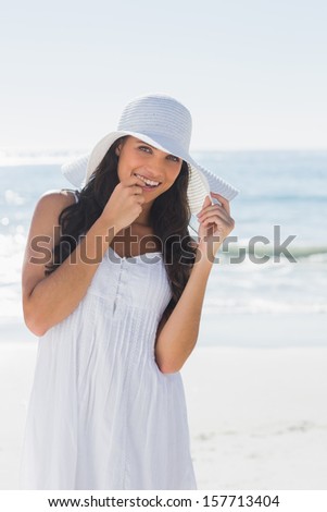 Happy brunette in white sunhat looking at camera at the beach