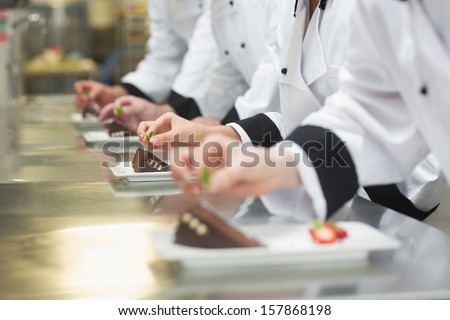 Team Of Chefs Garnishing Dessert Plates In A Busy Kitchen