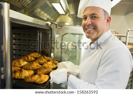 Mature Baker Smiling Proudly At The Camera Take Some Croissants Out Of Oven