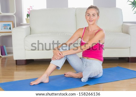 Sporty happy blonde sitting on blue exercise mat in bright living room