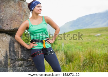 Pretty female rock climber leaning on rock face looking away in countryside