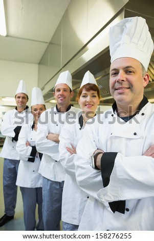 Team of happy chefs smiling at the camera in a kitchen wearing uniforms