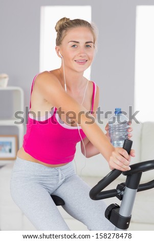 Sporty content blonde training on exercise bike listening to music in bright living room