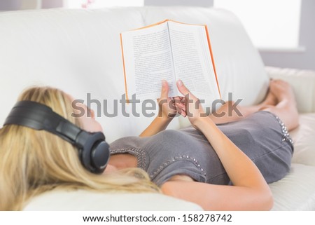 Casual pretty blonde lying on couch listening to music in bright living room