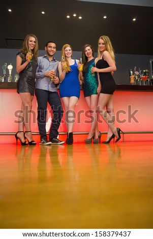Attractive friends standing at a bar holding beer looking at camera