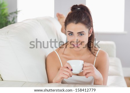Beautiful woman lying on a couch holding a cup in the living room