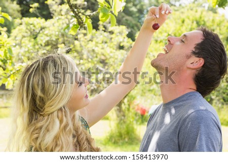 Blonde woman giving her boyfriend a cherry while laughing on a sunny day