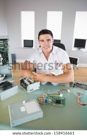 Good looking computer engineer sitting at desk smiling at camera in bright office