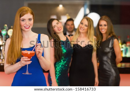 Attractive woman holding cocktail standing in front of her friends looking at camera