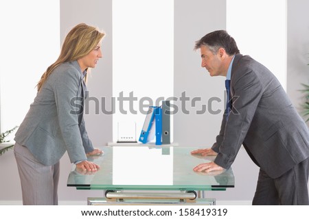 Two irritated businesspeople standing arguing on each side of a desk at office