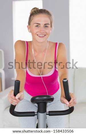 Portrait of sporty cheerful blonde training on exercise bike in bright living room