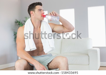 Attractive sporty man drinking from water bottle in bright living room
