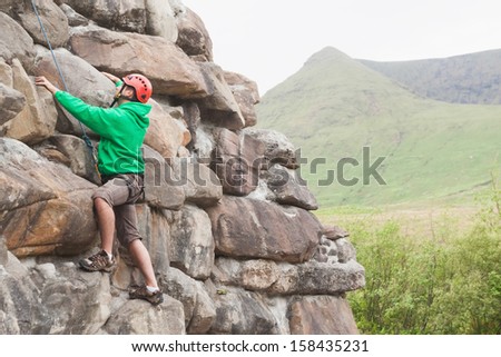 Focused man climbing a large rock face with mountains in the background