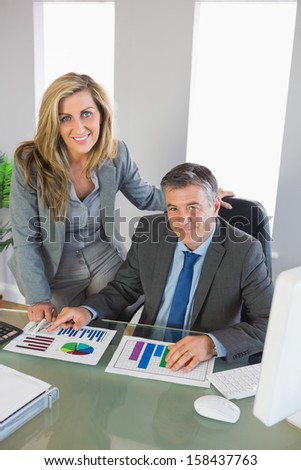 Pleased businesspeople smiling at camera studying figures at office