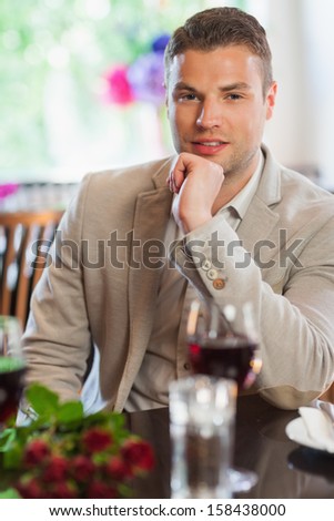 Smiling handsome man waiting for his girlfriend with a bouquet in restaurant