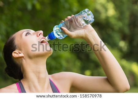 Fit woman drinking water from sports bottle outside on sunny day
