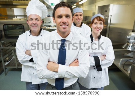 Restaurant Manager Posing In Front Of Team Of Chefs Smiling At Camera